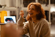 © Studio Marmellata - A young woman with curly red hair laughs heartily while sitting in a dimly lit room with a laptop open in front of her.