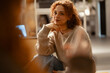 © Studio Marmellata - A young woman with curly red hair sits indoors, resting her chin on her hand, looking thoughtfully towards the viewer.