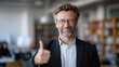 © Maksym - Professional education director smiling confidently and giving a thumbs-up gesture in a school classroom, soft depth of field, books and classroom elements subtly visible, neutral