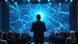 © Vadym - Man in suit speaks at tech conference before audience. Big screen shows futuristic network graphics. Speaker presents data. Event has bright stage lights and seats.