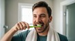 © andi - Smiling man brushing teeth with green toothbrush in bathroom, towel around neck