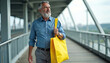 © Pete - Elderly man walks on bridge carrying bright yellow tote bag. He wears blue shirt grey pants. Modern city overpass background. Casual daily commute or shopping trip.