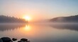 © Ad - Peaceful sunrise over a misty lake with tranquil water reflecting the soft morning light and distant trees.