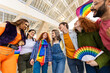 © Xavier Lorenzo - Happy LGBT friends holding rainbow fan and flag. Diverse young people laughing together at pride celebration. Community and equality concept.