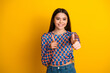 © deagreez - Bright smiling young mixed race woman gives thumbs up against a yellow background wearing a blue check shirt and jeans