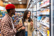 © unai - Diverse couple grocery shopping choosing food items in supermarket aisle