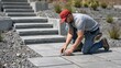 © NaesyaStudio - Focused man in red cap and work clothes meticulously installs grey paver stones for a new outdoor pathway, enhancing a home landscaping project with precision