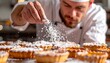 © Rakib - Chef meticulously garnishing tarts with powdered sugar in bakery.