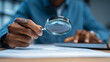 © Techno Stoks - man using a magnifying glass to highlight a glowing light bulb with question marks on a black background