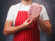 © mark_gusev - Masculine male butcher in white shirt and red and white classic stripe apron showing top quality T-bone steak in vacuum package for extra freshness of the product. Top price beef promotion.