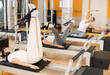 © JackF - Motivated young guy performing focused rehabilitation feet-in-strap exercises on Pilates reformer to relieve tension in hamstrings and build core muscles strength