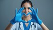 © Phannaporn - A single nurse wearing blue medical gloves, forming a heart shape with her hands, smiling gently with a warm
