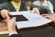 © pressmaster - Girl handing passport and approved visa application form to unknown woman across counter at visa center, background showing blurred people waiting