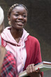 © wavebreak3 - African American teenage female and peer smiling, holding books at school, wearing red jacket