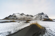 © Travel 'n' Lifestyle - View of stark black sand dunes meet icy white snow under towering, rugged mountains creating a mesmerizing contrast, Hofn, Iceland.