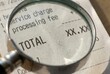 © Evgenia - Close-up view of a receipt under a magnifying glass highlighting the total amount, with service charge and processing fee details visible on the paper