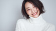 © bephoto - 女性が白いニットで穏やかに微笑む