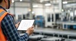 © Sim - A man in a high-visibility vest holding a tablet in a factory setting.