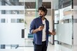 © Tetiana - A young Indian man holds a phone in his hand and opens the glass door of the office