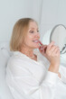 © neirfy - A cheerful woman 60s enjoys her dental hygiene routine at dentist, reflected in mirror sitting at dental office chair indoor light cabinet look at teeth toothy smile whitening result Healthcare caries