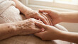 © Liana - Close-up of an elderly person's hands gently held by younger hands, symbolizing care, compassion, and the bond between generations. The image reflects warmth, support, and human connection.