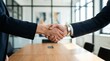 © irshad_mai - Two businessmen shaking hands in a modern office with a large wooden table and glass walls
