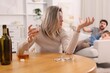 © New Africa - Alcohol addiction. Woman drinking whiskey at wooden table while her scared husband and daughter sitting on sofa indoors, selective focus