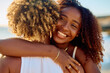 © we.bond.creations - Happy young woman joyfully embracing another person on a sunny beach, sharing a moment of genuine friendship and affection