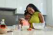 © Wavebreak Media - African mother and child hugging, whisking in kitchen in lime-green, coral tops with metal whisk