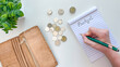 © Lisi4ka - A hand records expenses in a notebook labeled 'Budget.' Coins and an open leather wallet lie nearby. Concept of financial tracking, expense control, and personal budget management.