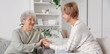 © Pixel-Shot - Mature woman with her mother holding hands on sofa at home