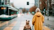 © Pinklife - An elderly figure in a bright yellow coat stands at a crosswalk, accompanied by a cuddly bear-like pet, waiting for a tram amidst an urban landscape in rainy weather.