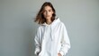 © Maryna - Young woman in loose white hoodie stands indoors against neutral grey backdrop. She wears minimal jewelry. Her casual style is modern and clean, perfect for fashion blogs or urban lifestyle content.