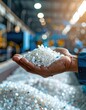 © Jaw - Close-up of hand holding recycled plastic flakes in a factory setting.