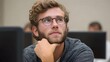 © Bussakon - A thoughtful young man with glasses and a beard sits in a classroom resting his chin on his hand and looking upwards
