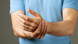 © SHARMIN - Man holding wrist in pain wearing blue shirt against gray background injury hand
