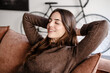 © luciano - Smiling relaxed serene pretty young woman feel fatigue lounge on comfortable sofa hands behind head rest at home, happy calm lady dream enjoy wellbeing in cozy home modern living room
