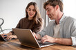 © luciano - Millennial couple sit at table browsing web with two laptop shopping online or studying, smiling young husband and wife work on computer at desk pay household bills or taxes in internet banking
