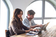© luciano - Millennial couple sit at table browsing web with two laptop shopping online or studying, smiling young husband and wife work on computer at desk pay household bills or taxes in internet banking