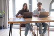 © luciano - Millennial couple sit at home browsing web with two laptop shopping online or studying, smiling young husband and wife work on computer at desk pay household bills or taxes in internet banking