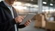 © forenna - Digital supply chain tracking app on a tablet held by a warehouse manager in an efficient distribution center. Sunlight streaming through large windows casting shadows on neatly organized stock and