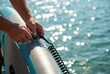 © Stitch - Man's hands attaching a coiled safety leash to an inflatable stand-up paddleboard on a sparkling sea.