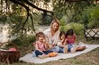 © Jelena - Mother enjoying picnic by the river with her three daughters