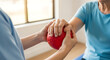 © RATUL HASAN - Physiotherapist helping senior woman with arm exercise using a red stress ball at home