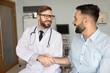 © fizkes - Shared recovery success. Joyful smiling young doctor and patient sit together on couch in clinic office shake hands celebrating successful therapy collaboration positive results of treatment teamwork