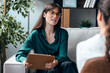 © nenetus - Female psychologist giving therapy to a patient while taking notes, sitting on the couch in the psychology office