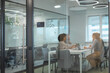 © ty - A view through a glass partition shows a modern, busy office interior. Business people are working at desk.