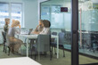 © ty - A view through a glass partition shows a modern, busy office interior. Job interview process is in office. Human resources, meeting and group of hiring candidates for vacancy.