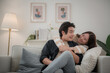 © surachetkhamsuk - Happy young Asian couple hugging, sitting on cozy couch together, overjoyed laughing woman and man having fun, enjoying leisure time, relaxing on sofa in living room at home
