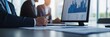 © oksa_studio - Business professionals discussing market trends and financial performance during a corporate meeting, pointing at charts and graphs on a computer monitor while reviewing documents on the desk